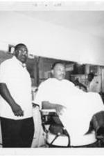 Martin Luther King Jr. sits in a chair at a barbershop.