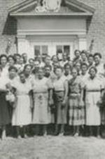A group portrait of unidentified people stand in front of a building.