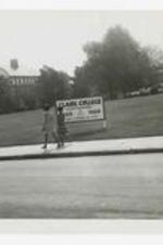 Two women walk on a sidewalk by a sign that reads "Clark College Centennial, 1869, 1969, 100 years of progress and Service" on campus.