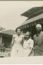 A group of two women and one man stand together outside a house.