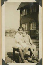 Two girls sit on a bench outside of the home.