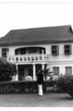 An unidentified man stands in front of a large house.