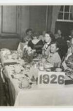 Women and a girl sit at a banquet table, on sign: 1926. Written on verso: Banquet incl. Class of 1926 table incl. unidentified women and Grace Holmes DeLorme (left) ca. 1940s.
