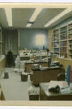 Two unidentified people work in an office surrounded by books.