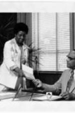 Minnie Wright and Dr. Grant Shockley hold an piece of paper at Dr. Shockley's desk. Written on verso: Pacs. See. Minnie Wright &amp; Dr. Shockley.