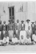 A group of men and boys stand in front of a building. Written on verso: Mr. Mooney, native commissioner, graduates and students of Garraway Mission School in front of church.