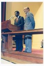 View of President Hugh Gloster with unidentified person at podium.
