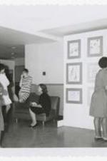 Five women look at art on a wall and enteract with each other at an art exhibit.