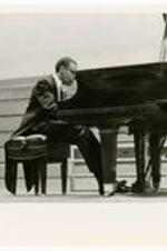 An unidentified man wearing a tuxedo suit plays a grand piano.