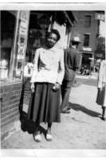 An unidentified woman stands on the sidewalk next to a store.