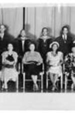 Group portrait of men and women on a stage. Possibly a graduation.