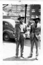 Two unidentified men in suits stand on a street next to a car in Welch, West Virginia.