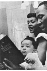 Coretta Scott King and her husband Martin Luther King, Jr. look at a book with their daughter Yolanda.
