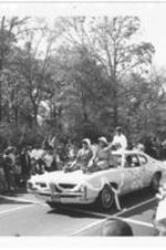 Two attendants ride on the front of a car while JoAnn Bass, Miss Gaines Hall, rides on the back during the Morris Brown Homecoming Parade.