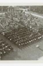 An aerial view of graduates and other men and women in sitting on folding chairs in the audience of commencement.