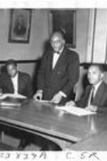 Three men work behind a large desk. Written on verso: Pre-Alumni Officers. Left to Right: James Bradley, '59; Therman Taylor, '60; Samuill (?) Walker, '59.