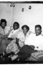 Four unidentified people sit on a striped couch in a living room.