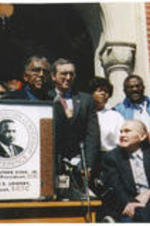 Joseph E. Lowery stands at a podium during a press event in front of the St. Jude Educational Institute with George Wallace. The event was to mark the 30th anniversary of the Selma to Montgomery March.