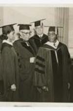 Three men and three women, wearing graduation caps and gowns, at commencement.