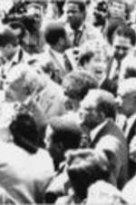 Southern Christian Leadership Conference President Joseph E. Lowery is shown standing with Nelson and Winnie Mandela (at middle center of photo) amongst a crowd of people and the press.
