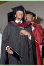 An unidentified I.T.C. graduate receives a red hood with his diploma.