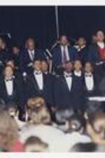 Men and women, wearing suits with bow ties, sing at convocation.