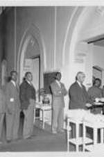 An unidentified man serves a drink to an unidentified man as other men stand in line at the dining hall.