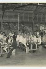 Indoor view of men and women seated at tables. Written on verso: Lay retreat Aug. 8-9, 1953.