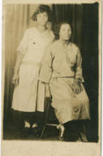 An unidentified woman sits on a stool while an unidentified girl behind her stands.