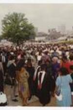 A large crowd of people gathered outside, including graduates wearing graduation caps and gowns.