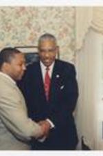 Wynton Marsalis and Thomas W. Cole, Jr. shake hands in a dining room with floral wallpaper.