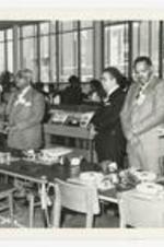 Indoor view of men and women standing among tables with turn tables and headphones. Written on verso: "Ribbon cutting ceremony Learning Resource Center March 1983; Dr. Sidney Estes (3 from right)".