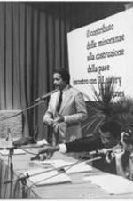 Joseph E. Lowery is shown pouring a drink while another panelist speaks at the Meeting Per L'Amicizia Fra I Popoli, the Meeting of Friendship Among the People, in Rimini, Italy. For more details about this event, see page 43 of the September-October 1980 SCLC Magazine: http://hdl.handle.net/20.500.12322/auc.199:07014.