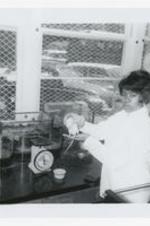 A young women holds a rat at a laboratory counter a scale and other science equipment in a classroom.