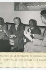 Four men sit on a sofa and talk. Written on recto: Le president de la republique en conversation avec le Dr. Robinson, le juge Douglas et l'ambassadeur Kaiser.