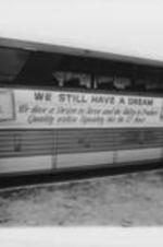 A charter bus dropping off attendees at the 23rd Annual Southern Christian Leadership Conference (SCLC) Convention is shown with a banner on the side for the SCLC Chicago Metropolitan Chapter stating "We Still Have A Dream". Written on verso: Cleveland '80