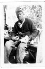An unidentified man holding a puppy sits on a house porch.