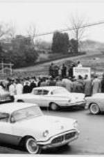 A group gathers outside by a row of cars for the ITC groundbreaking dedication. Written on verso: Dedication service for the new site February 4, 1960.